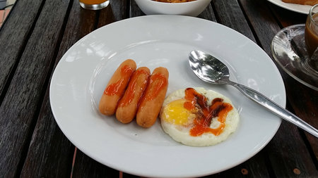 Fried sausages and fried egg in white dish on wooden tableの写真素材