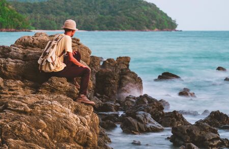 A man on the rock with backpack and looking sea. concept for adventure and travel sea in  summer vacations and outdoor aloneの写真素材
