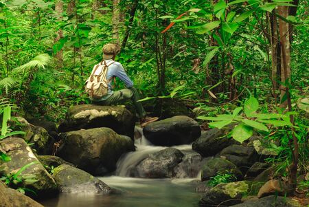 Man sitting on rock in rainforest with backpack among Small streams flow through abundant tropical forest concept summer vacations outside alone into the wild of Thailand,Phang Nga,Koh Yao Yaiの写真素材