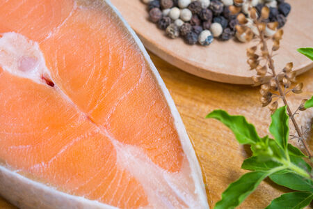 Salmon steak on wooden board with peppercorn and brasil leafの写真素材