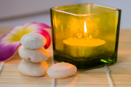 Candle and white stones with flower on bamboo matの写真素材