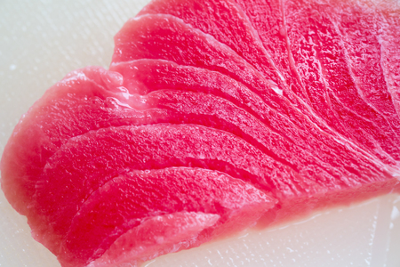 Closeup piece of tuna fillet on white cutting boardの写真素材