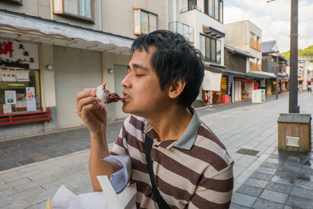 Fukuoka, Japan - September 26 2014: Man eating Moji on the street to Dazaifu Tenmangu shrine.のeditorial素材