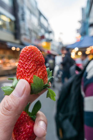 Strawberry in hand with the market backgroundの写真素材