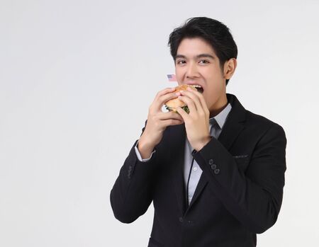 Stylish Asian young and handsome business man wearing dark suit eating burgur with American flag for.Independence day.4th July.の写真素材