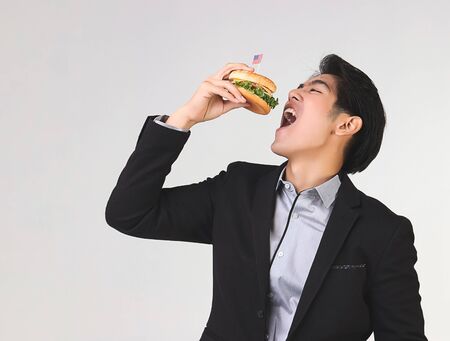 Stylish Asian young and handsome business man wearing dark suit eating burgur with American flag...