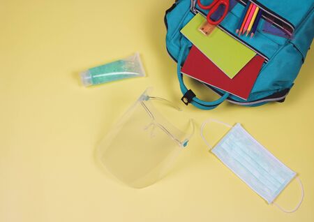 COVID-19 prevention while going back  to school  and new normal lifestyle concept.Top view of backpack with school supplies , surgical mask,face shield and alcohol sanitizer hand gel on yellow background with copy space.の写真素材