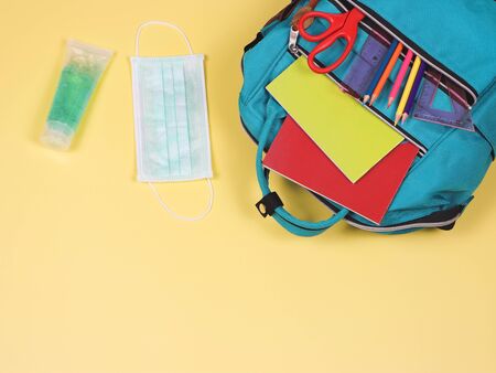 COVID-19 prevention while going back  to school  and new normal  concept. Top view of backpack with school supplies , surgical mask and alcohol sanitizer gel on yellow background with copy space.の写真素材