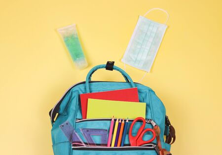 COVID-19 prevention while going back  to school  and new normal  concept. Top view of backpack with school supplies , surgical mask and alcohol sanitizer gel on yellow background with copy space.の写真素材