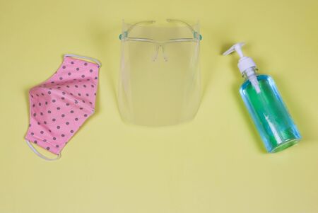 Coronavirus or COVID-19 prevention and new normal lifestyle concept. Top view of face shied  , alcohol hand sanitizer gel and pink polka dot fabric  face mask  on yellow background.の写真素材