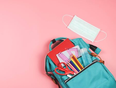 COVID-19 prevention while going back  to school  and new normal  concept. Top view of backpack with school supplies , surgical mask and alcohol sanitizer gel on pink background with copy space.の写真素材