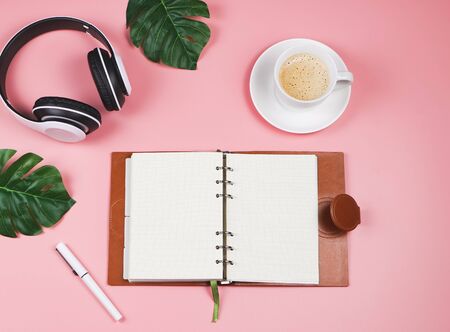 Morning routine concept.Top view or flat lay  of opened notebook , white headphones and cup of coffee on pink background decorated with tropical monstera leaves.の写真素材