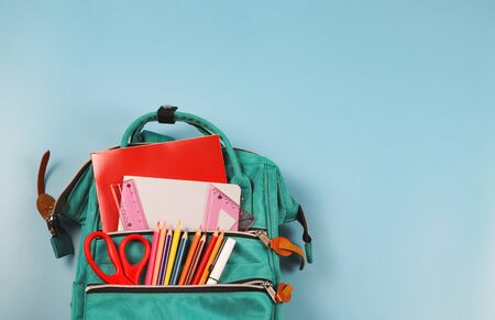 Back to school concept.Top view of green backpack with school supplies on blue  background with copy...