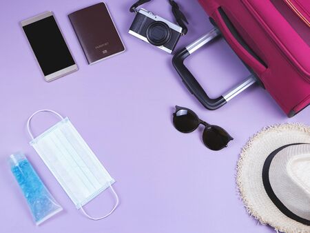 COVID-19 prevention while traveling and new normal lifestyle concept. Top view of surgical  face masks, alcohol  sanitizer gel and travel accessories on purple  background with copy space.の写真素材
