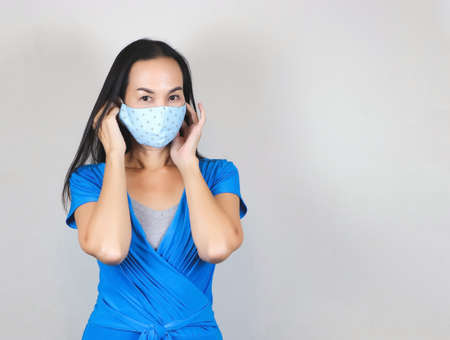 Beautiful Asian woman wearing blue polka dot hygienic mask and blue dresst,touching her mask and...
