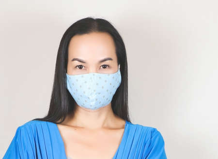 Close up image of beautiful Asian woman wearing blue polka dot  hygienic mask and blue dress,...