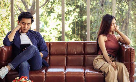 Young and attractive Asian couple spend good time at home , a man sitting on the floor with computer laptop on table while his girlfriend lying on sofa behind , giving high five.work from home conceptの写真素材