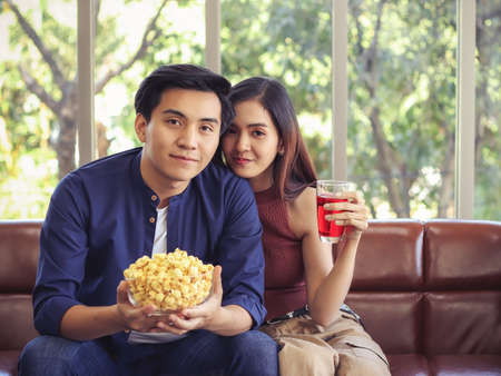 Attractive Young Asian couple sitting close together  on couch in living room with computer laptop on woman's lap , a man hugging her and woman looking at camera with finger on lips.の写真素材
