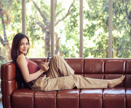 Young Asian couple sitting on couch in living room, a man playing game on smart phone while woman pouting to him.の写真素材
