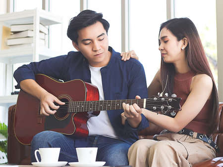 Young Asian couple sitting on couch in living room, a man playing game on smart phone while woman...