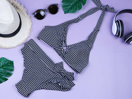 Travel and summer holiday concept, top view of  black and white stripe pattern  bikini swimsuit and women's vacation accessories items  on purple background with tropical monstera leaves.の写真素材