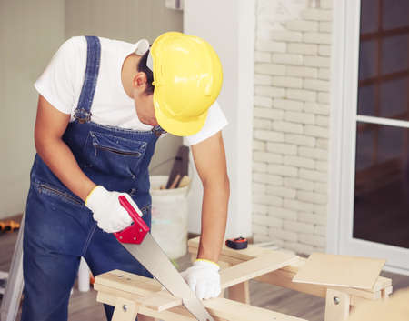 Handsome young Asian repairman wearing yellow safety helmet ,working in wood workshop with white...