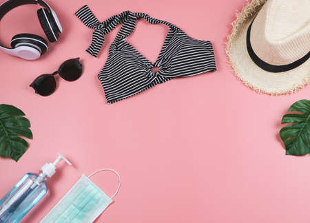 COVID-19 prevention , summer and new normal concept, top view of   bikini swimsuit and women's vacation accessorieswith surgical mask and sanitizer gel  on pink background with monstera leaves.の写真素材