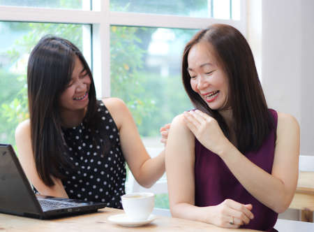 Two attractive Asian tourist women wearing hat sitting together in coffee shop  with camera in one...