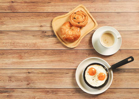 Top view of break fast set , fried eggs in pan , cup of coffee and  danish pastry and Croissant on wooden background.の写真素材