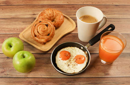 Healthy breakfast set , fried eggs , lattee coffee, orange juice ,croissant and danish pastry and two apples on wooden table. Selective focus.の写真素材