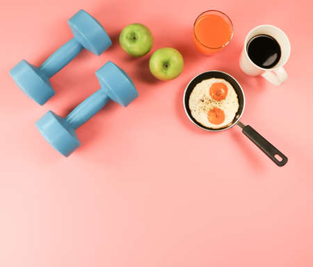 Top view of fried eggs in pan , orange juice , apples , black coffee and blue dumbbells on pink background .healthy lifestyle concept. copy space.の写真素材