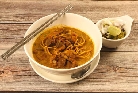 Khao Soi , Traditional Northern Thai curry noodles with pork on wooden table.の写真素材