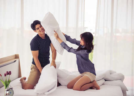 Young happy Asian couple beat the pillows on the bed in a bedroom at home.の写真素材