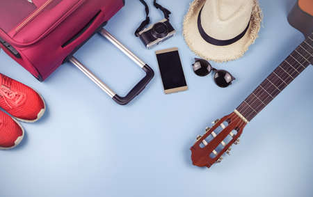 Flat lay of traveler accessories ,  hat , mobile phone, guitar,camera,sun glasses, sneakers and pink suitcase on blue background. travel concept.の写真素材