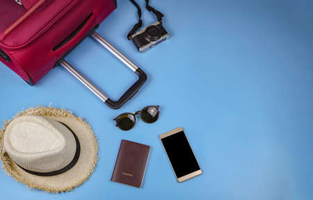 Flat lay of traveler accessories , passport , hat , mobile phone, camera,sun glasses and pink suitcase on blue background. travel concept.の写真素材