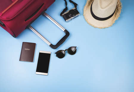 Flat lay of traveler accessories , passport , hat , mobile phone, camera,sun glasses and pink suitcase on blue background. travel concept.の写真素材