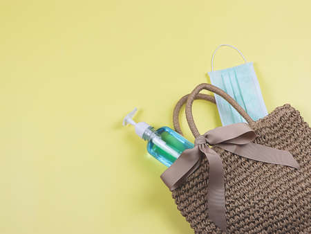 COVID-19 prevention and new normal concept, top view of   woven bag with  surgical mask and sanitizer gel   on yellow  background with copy space.の写真素材