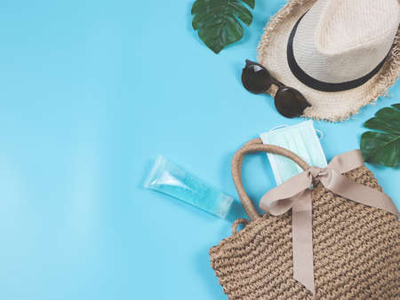 COVID-19 prevention , travel and new normal concept, top view of   woven bag with  sanitizer gel , surgical fabric  face mask  and women's vacation  accessories on blue  background.の写真素材