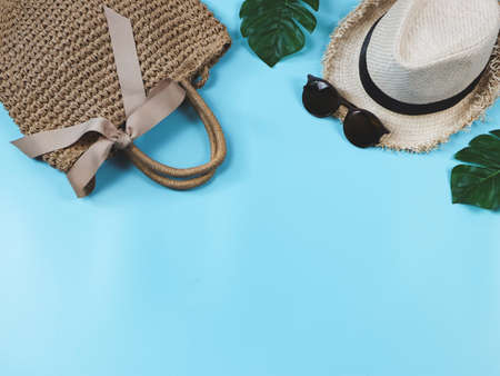Travel and summer holiday concept, Women's vacation accessories items (woven bag,hat and sunglasses)on blue background with tropical monstera leaves..top view with copy space.の写真素材