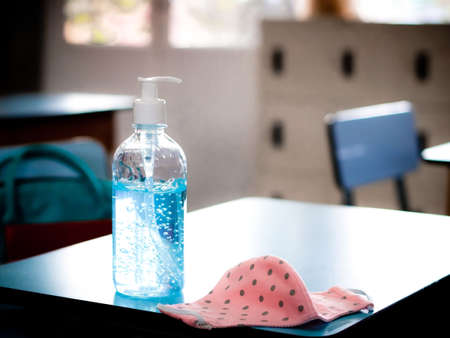 Covid-19 prevention , back to school,new normal concept.Alcohol sanitizer  hand  gel and pink polka dots fabric mask folded on school desk in  the classroom .の写真素材