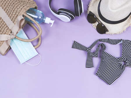COVID-19 prevention , travel and new normal concept, top view of   woven bag with  sanitizer gel  and surgical  face masks  with woman's vacation accessories on purple  background with copy space.の写真素材