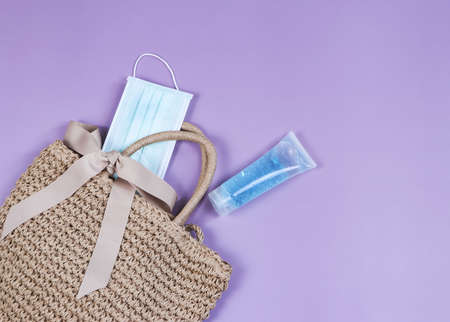 COVID-19 prevention , travel and new normal concept, top view of   woven bag with  sanitizer gel  and surgical  face masks  on purple  background with copy space.の写真素材