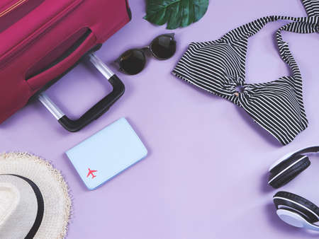 Travel and summer holiday concept, top view of  black and white stripe pattern  bikini swimsuit , passport and women's vacation accessories items  on purple  background with tropical monstera leaves.の写真素材