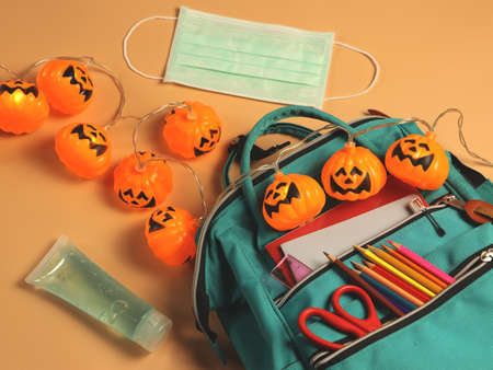 Top view of backpack with school supplies , medical mask , sanitizer gel and Halloween pumpkin lights on orange background.COVID-19 prevention,Education halloween and new normal concept.の写真素材