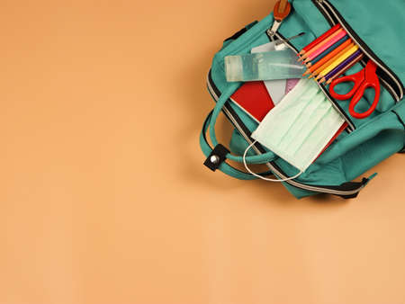 Top view of backpack with school supplies , surgical mask and alcohol sanitizer gel on orange background with copy space. COVID-19 prevention while going back  to school  and new normal  concept.の写真素材