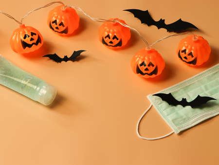 Top view of Halloween pumpkin lights , black paper bats,medical mask and alcohol sanitizer gel on orange background. Halloween , COVID-19 prevention and new normal concept.の写真素材