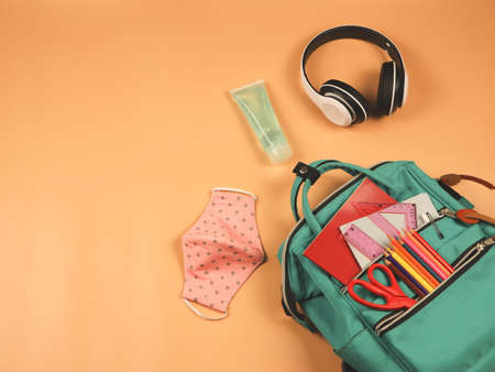Top view of backpack with school supplies ,headphones, pink polka dot fabric masks and sanitizer gel...
