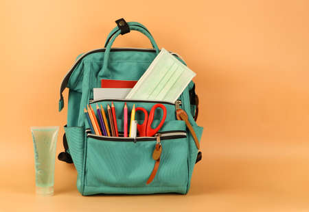 Front view  of green backpack with school supplies , medical mask and alcohol sanitizer gel on orange background with copy space.COVID-19 prevention while going back  to school  and new normal  concept.の写真素材