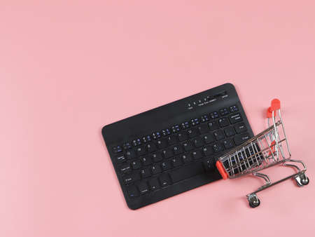 Top view or flat lay of computer keyboard with shopping cart on pink background with copy...