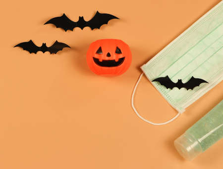 Top view or flat lay of Halloween pumpkin , black paper bats,medical mask and alcohol sanitizer gel on orange background. Halloween , COVID-19 prevention and new normal concept.の写真素材